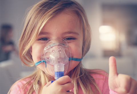 Young girl with oxygen mask smiling and giving a 'thumbs up'