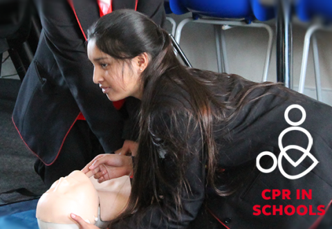 A teen in school uniform gets ready to do CPR on a manikin
