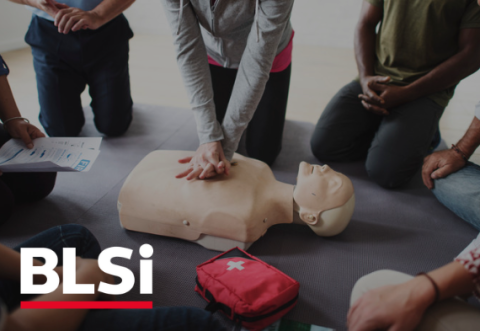 An image of people surrounding a manikin which is being given CPR by a person in a grey jumper. The BLSi logo is on the bottom right-hand side.