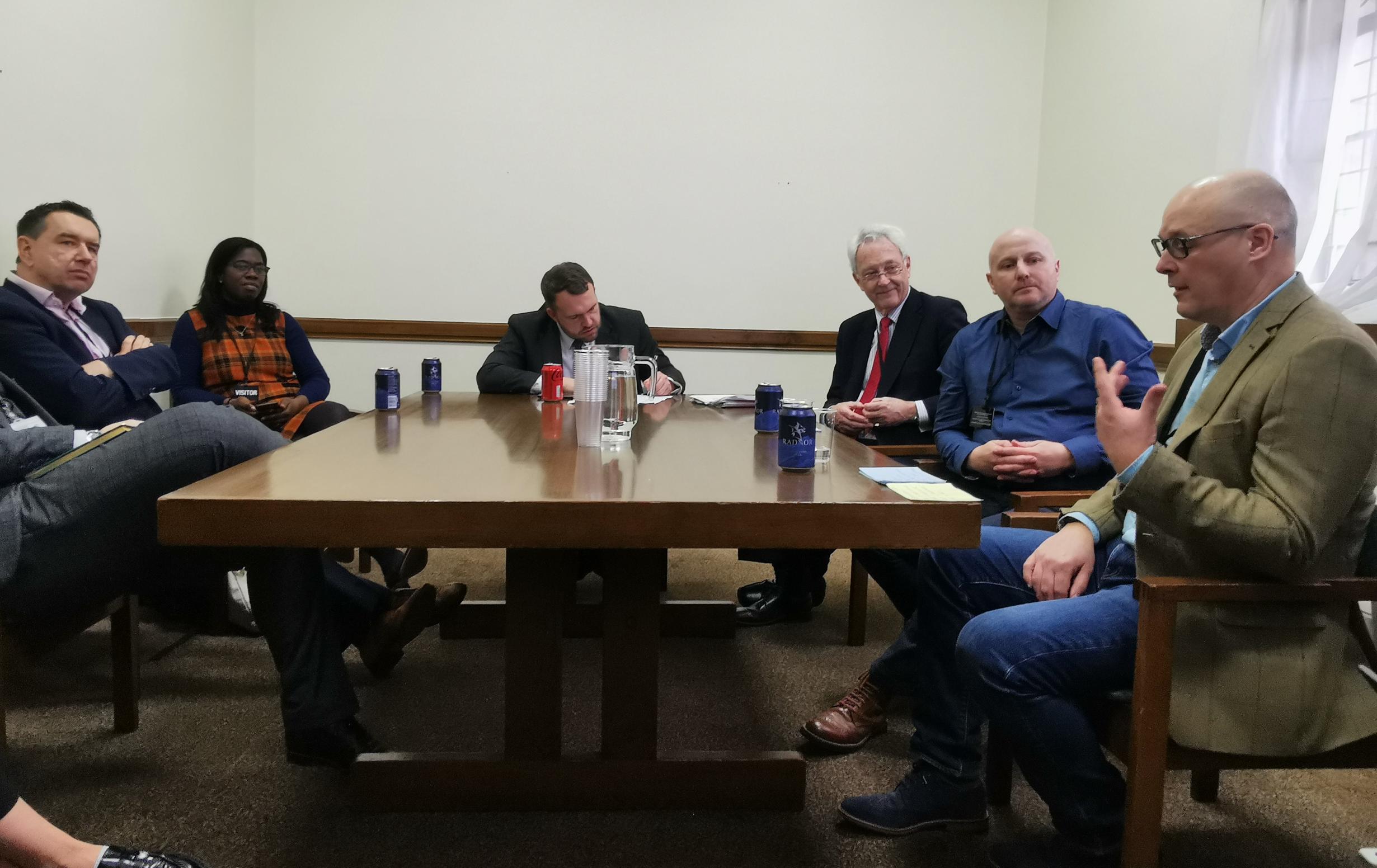 A diverse team of people sitting around a wooden table at the evidence session