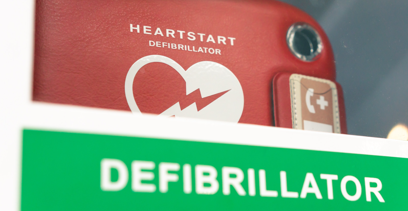 Image of a Red Defibrillator behind glass with a green label saying 'Defibrillator' on it