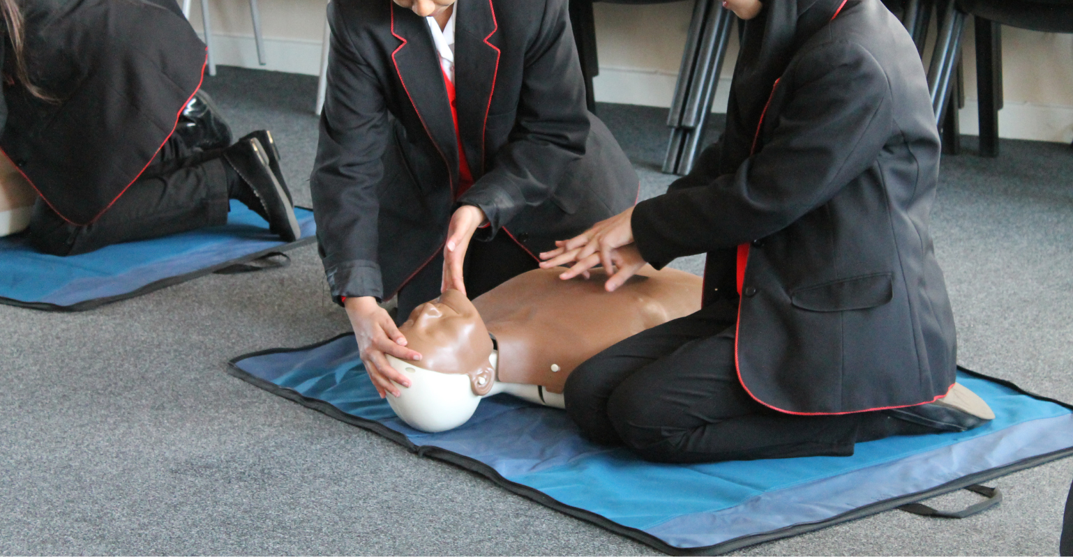 2 school students practising lifesaving on a dummy