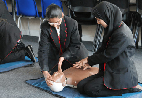 two students practicing CPR on a manikin