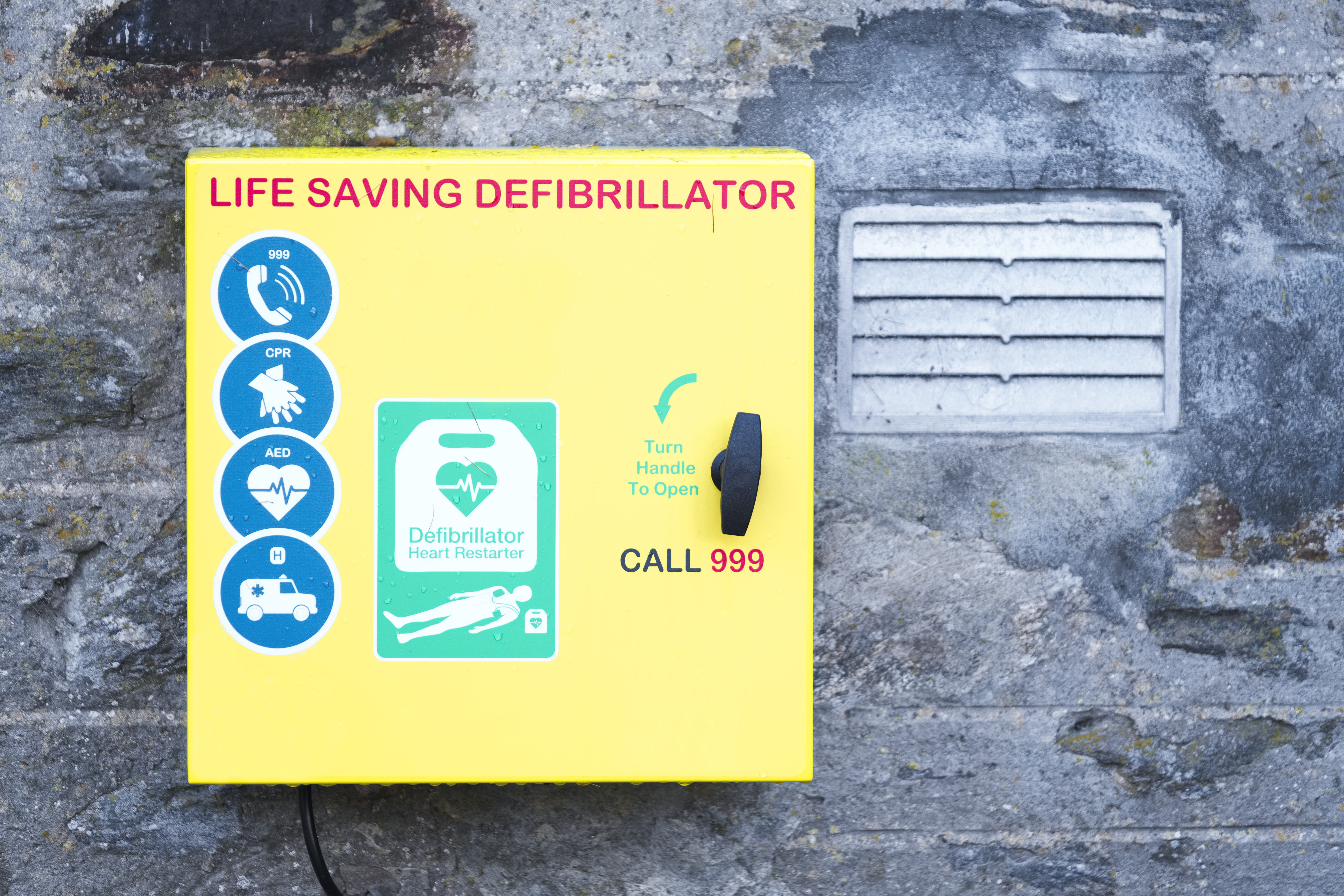 yellow defib cabinet mounted on a wall outside