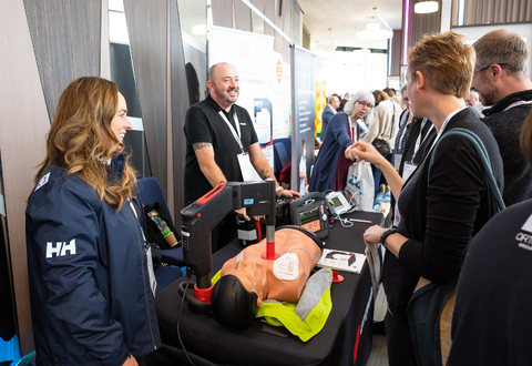 two representatives from a medical equipment company demonstrating something on a CPR manikin to attendees at a conference
