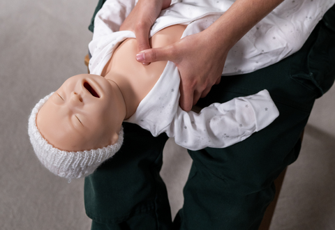 person performing chest compressions on a baby training manikin