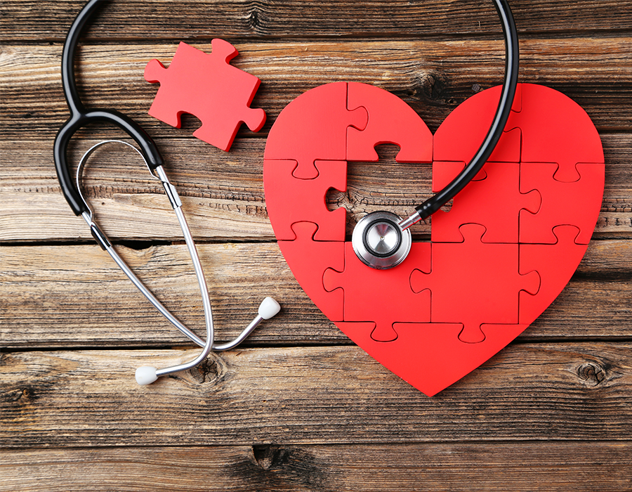 Stethoscope with puzzle in the shape of a heart on wood background.