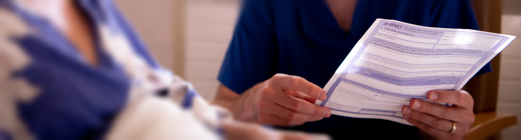 A patient in bed is shown a ReSPECT form by a health care professional