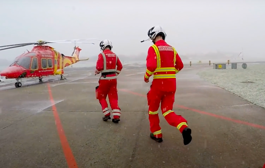 Two men in red responder uniforms running to a helicopter