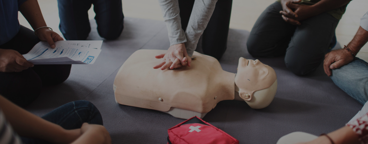 A diverse group of people around a manikin watching a CPR demonstration