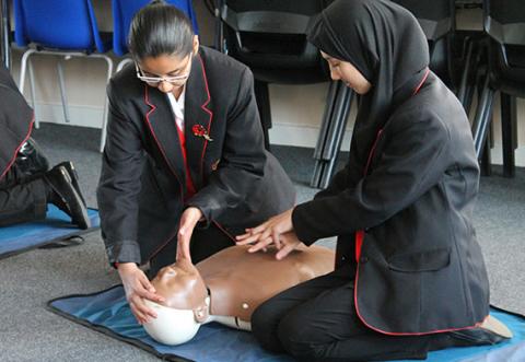 Two girls learn CPR using a manikin