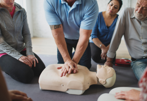Man showing how to do CPR on a mannequin to a group watching. 