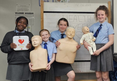 primary school children posing for photo holding CPR manikins