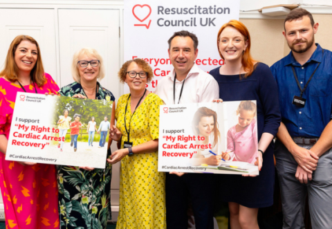 A group of people smiling for a photo holding up signs about the my right to cardiac arrest recovery campaign