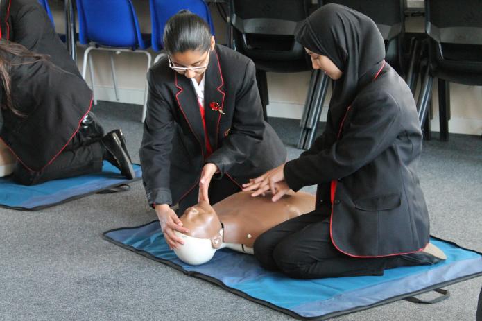 Two teenage students practice CPR on a manikin in the classroom