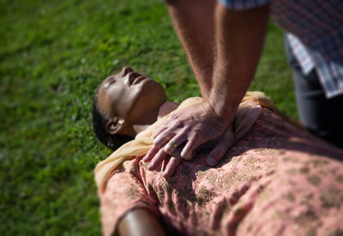 A bystander provides CPR to a woman collapsed in a park