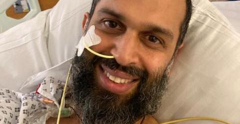 An image of Asad lying in a hospital bed, smiling