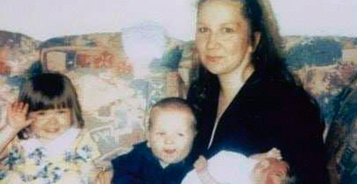 An old, grainy photograph of a woman sitting on a sofa with two young children