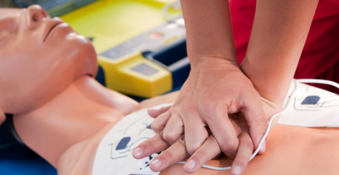 Someone demonstrating CPR on a mannequin while using a defibrillator