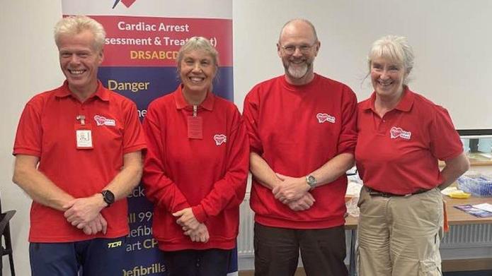 Four people smiling in red tshirts with the Heartstart Malvern logo.